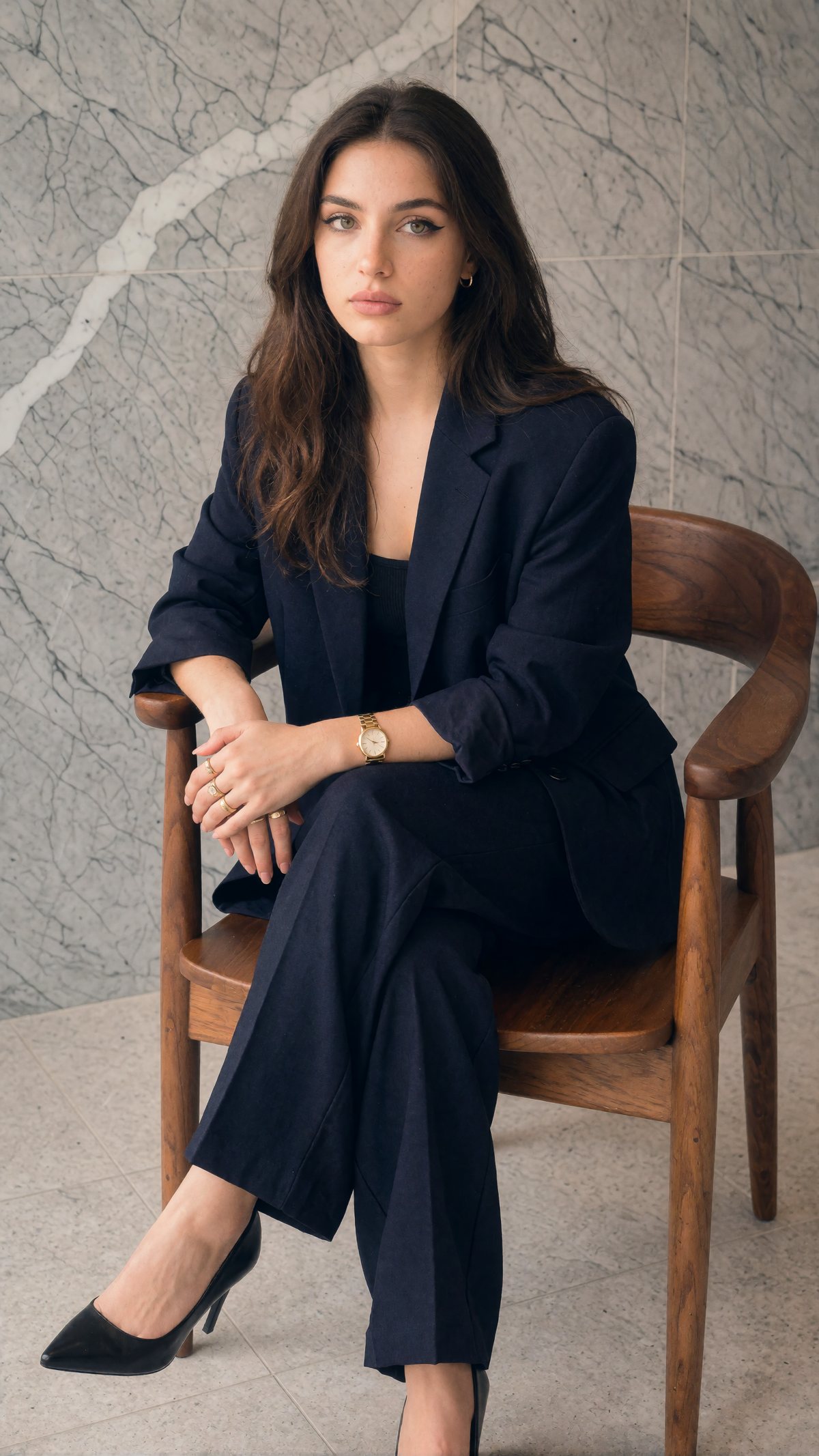 Sofia, StudioLine's AI-generated presenter, in a navy suit on a wooden armchair